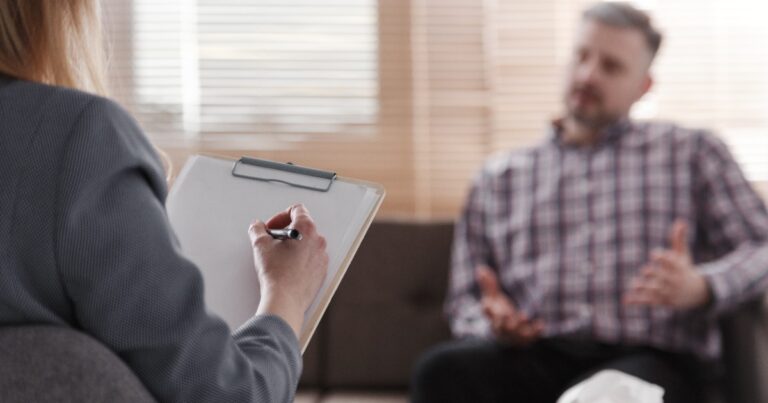 Female therapist taking notes while conducting therapy session with male client in comfortable office setting
