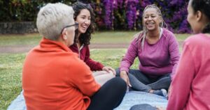 Diverse group of women laughing and connecting in supportive outdoor gathering, representing community support for bipolar disorder recovery and mental health healing