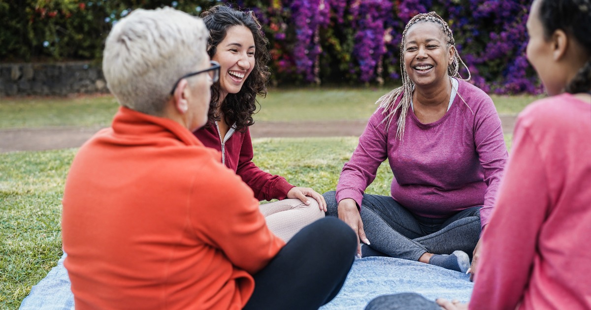 Diverse group of women laughing and connecting in supportive outdoor gathering, representing community support for bipolar disorder recovery and mental health healing